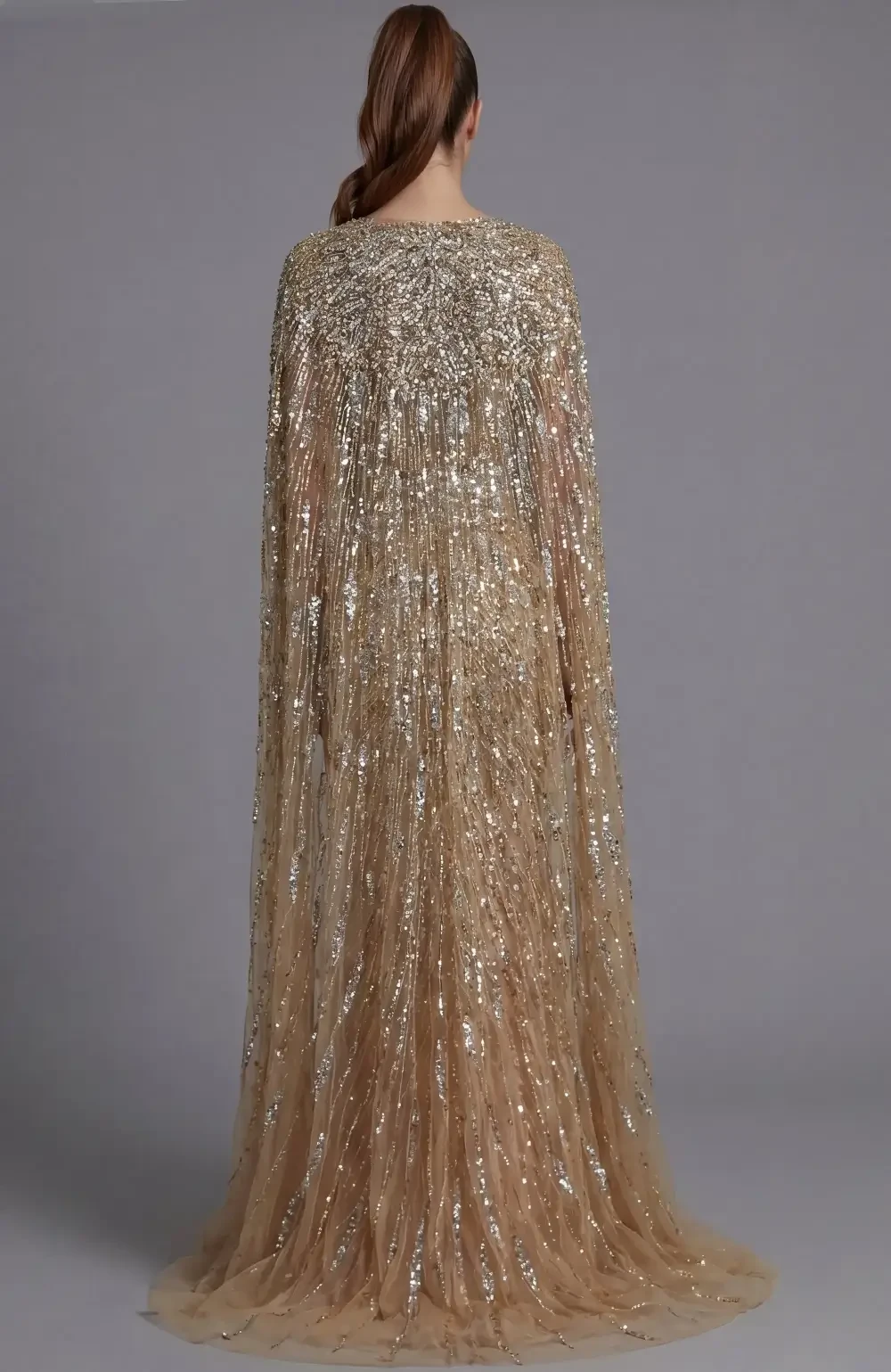 A woman wearing a glamorous, fitted, gold sequin gown with a plunging neckline and a flowing cape-like detail.