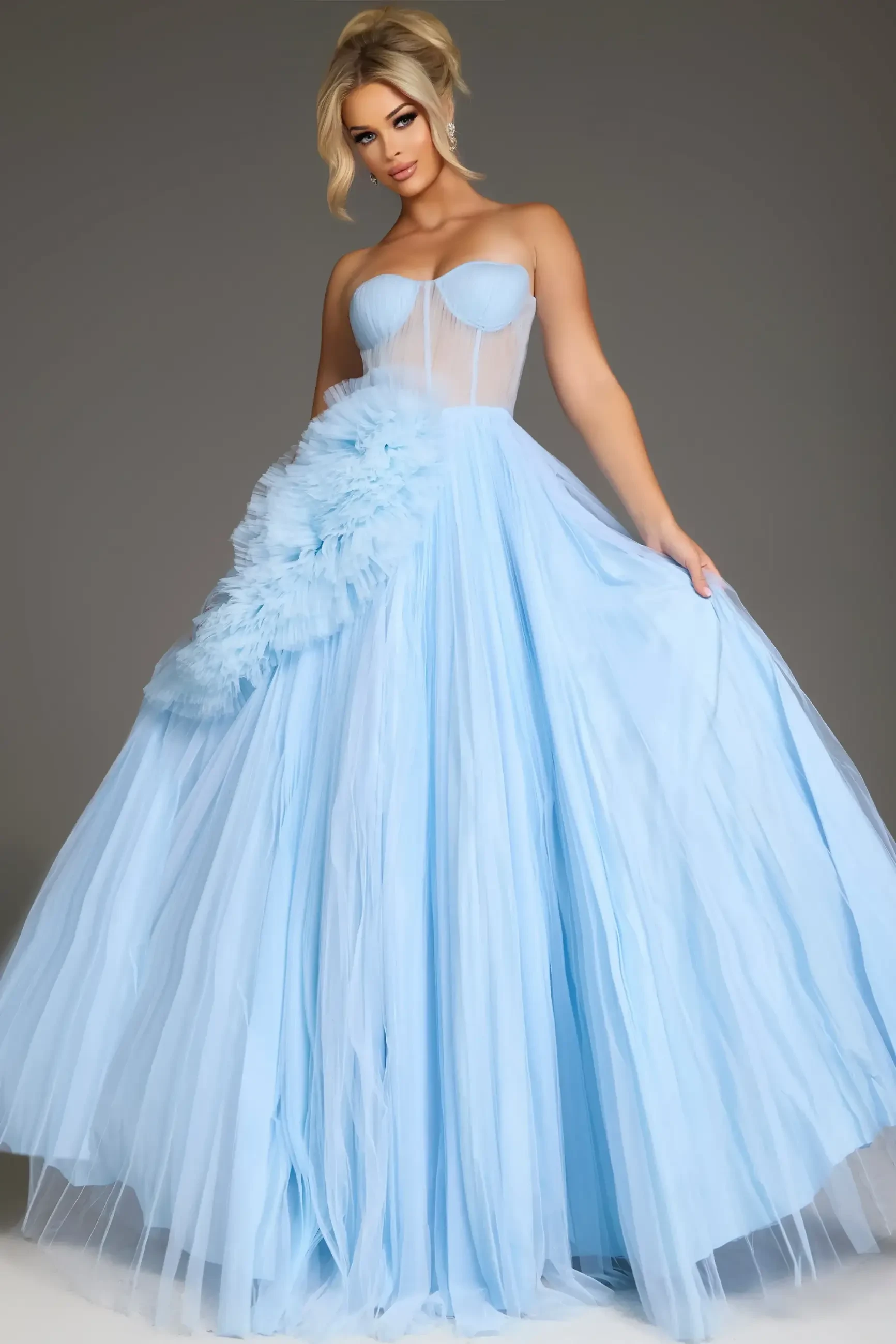 A woman in an elegant light blue gown with a strapless bodice and full skirt adorned with ruffles poses confidently against a gray background.