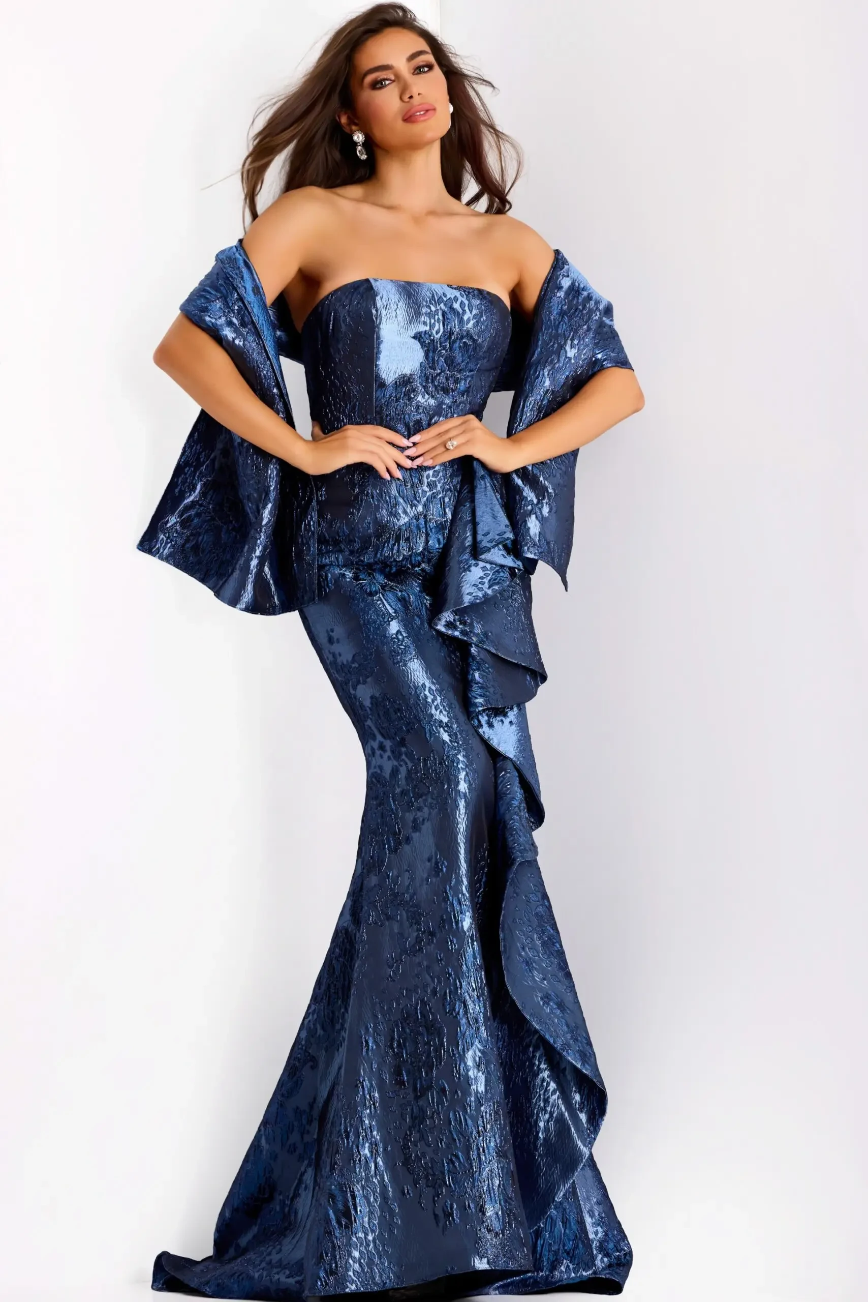 Model is wearing a strapless mermaid gown with side ruffles, fitted bodice and hips, a flared knee-length skirt, and metallic pleated detailing