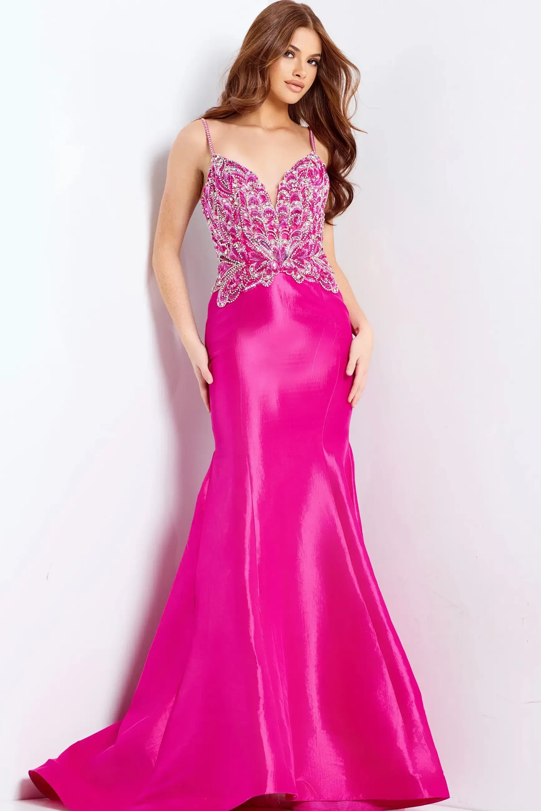 A woman wearing a pink evening gown with embellishments at the bodice, standing against a white background.