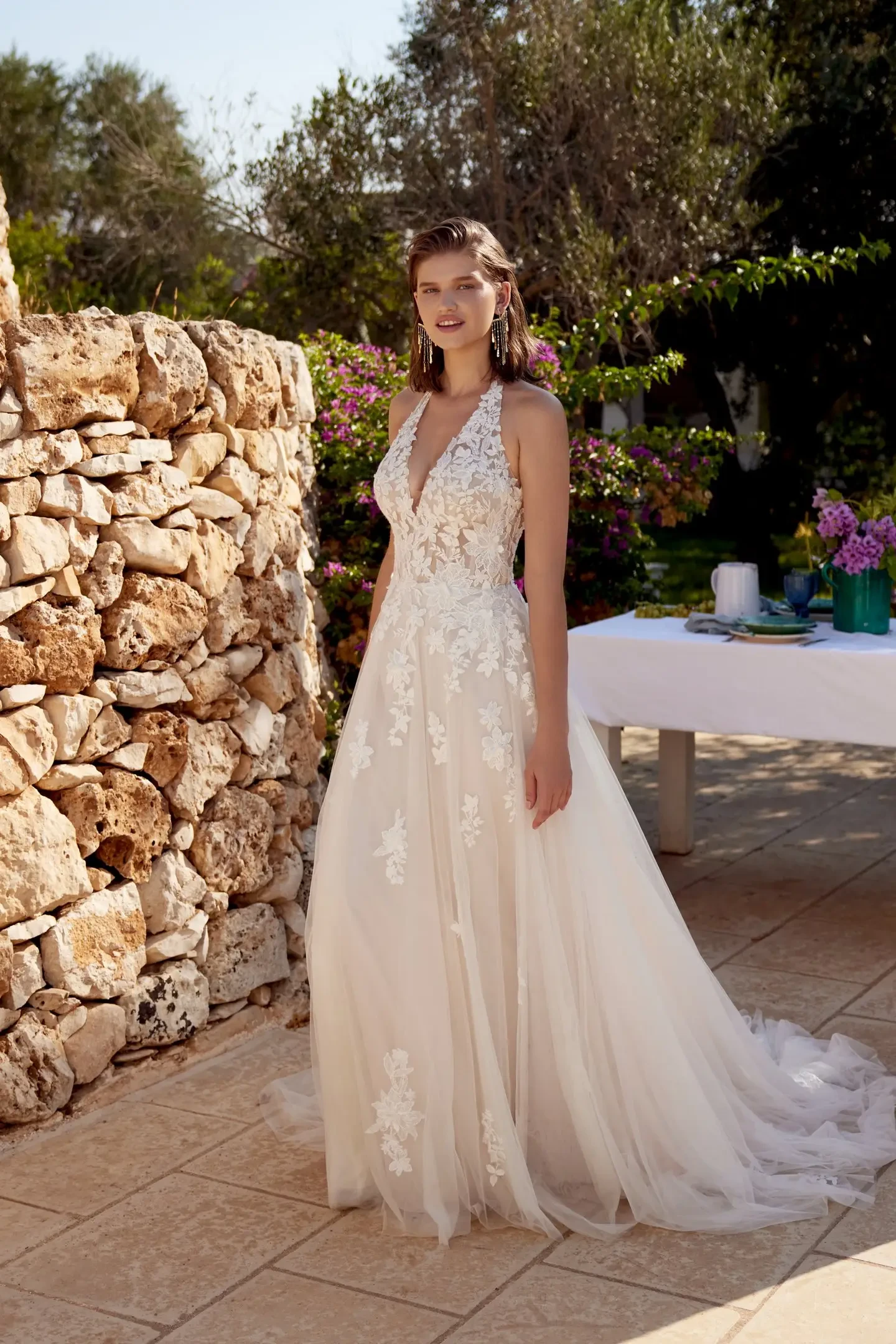 Model is wearing a sleeveless halter A-line wedding gown with a sheer back and airy tulle skirt