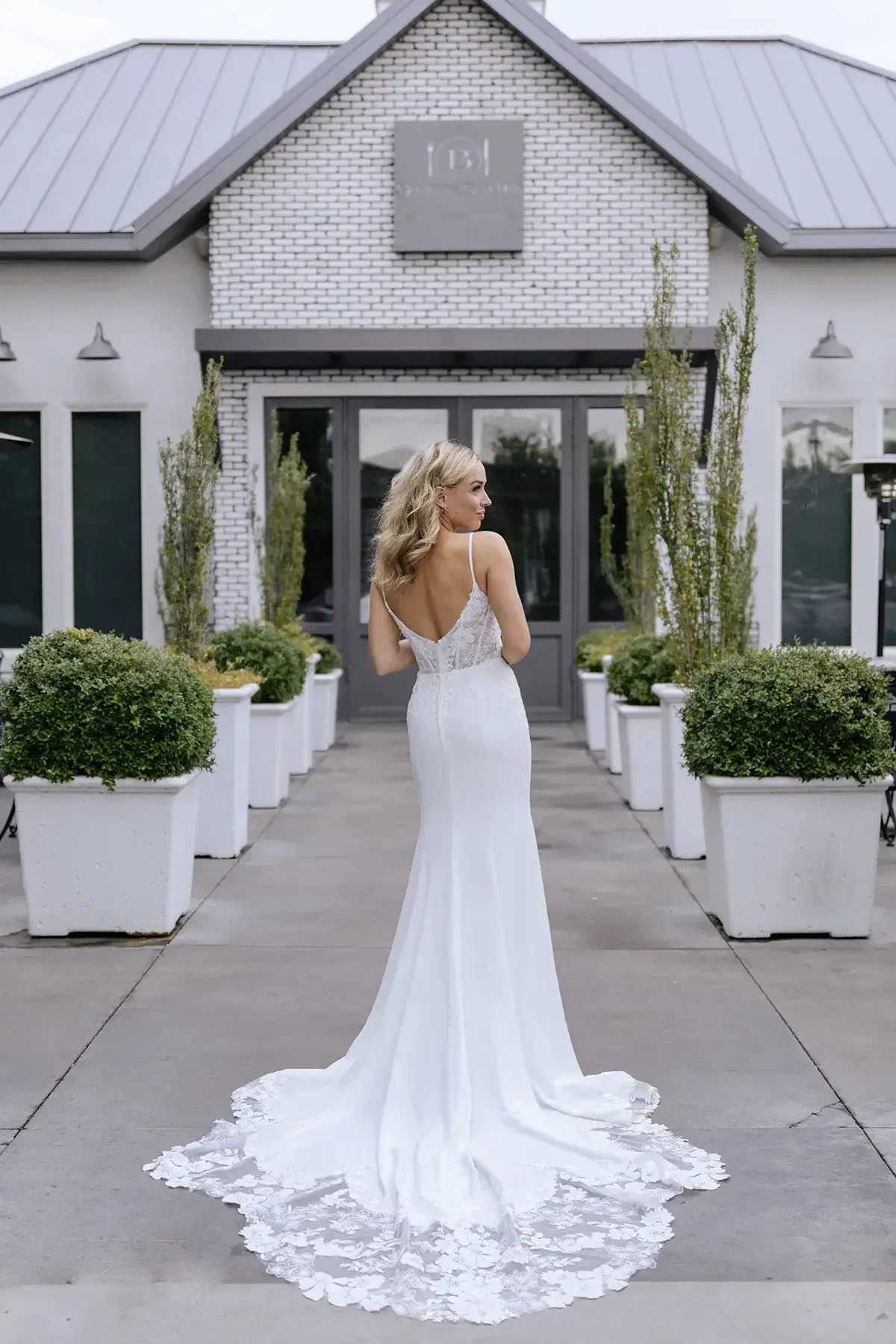Model is wearing a romantic yet edgy gown with a sheer floral lace bodice, spaghetti straps, square neckline, and a fitted crepe skirt with a lace train.