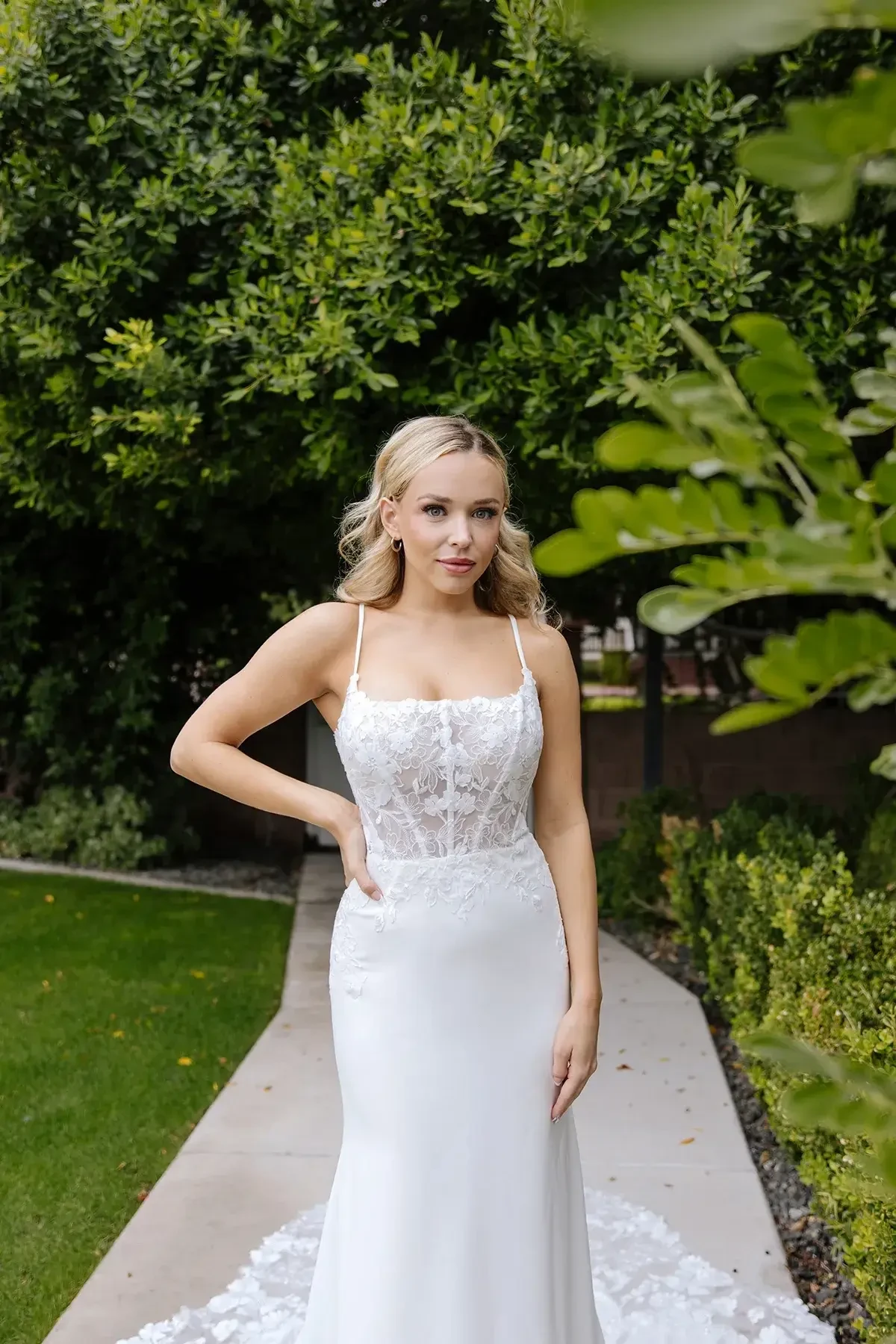 Model is wearing a romantic yet edgy gown with a sheer floral lace bodice, spaghetti straps, square neckline, and a fitted crepe skirt with a lace train.