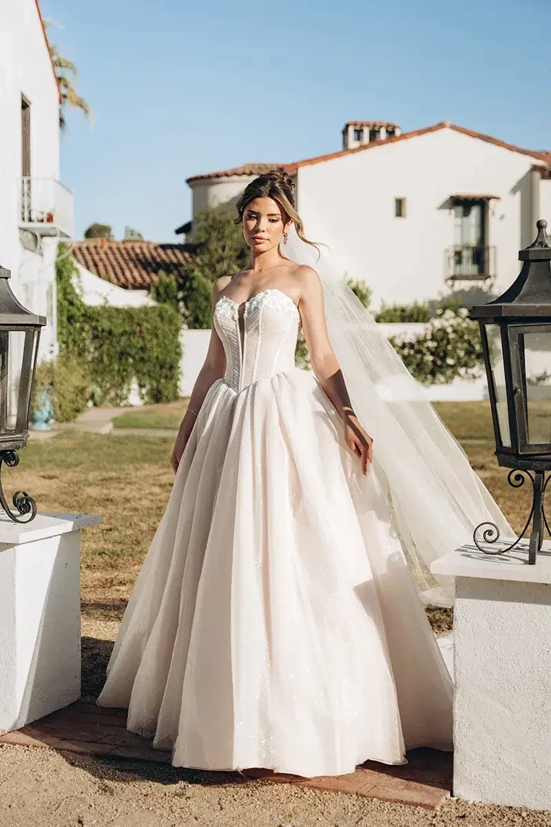 Model is wearing a dramatic strapless ballgown with a sweetheart neckline, ruched bodice, visible corset boning, and a full sparkling tulle skirt.
