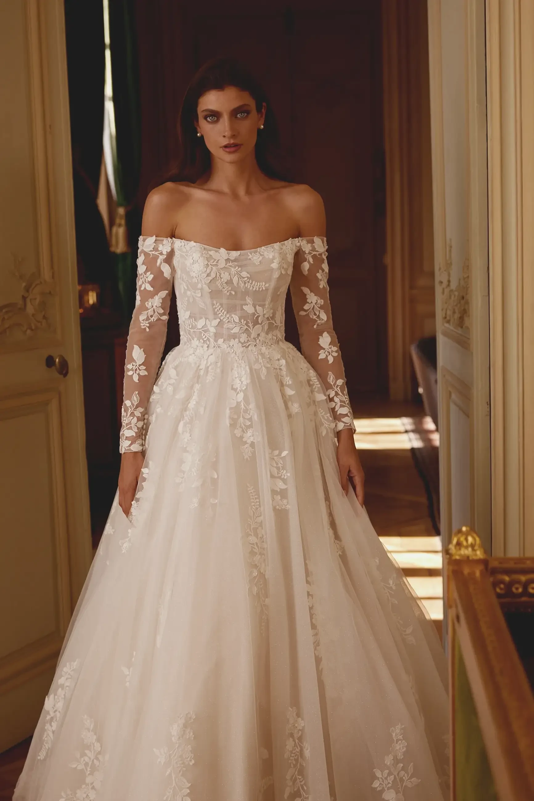 Model is wearing an off the shoulder long sleeve ball gown wedding dress
