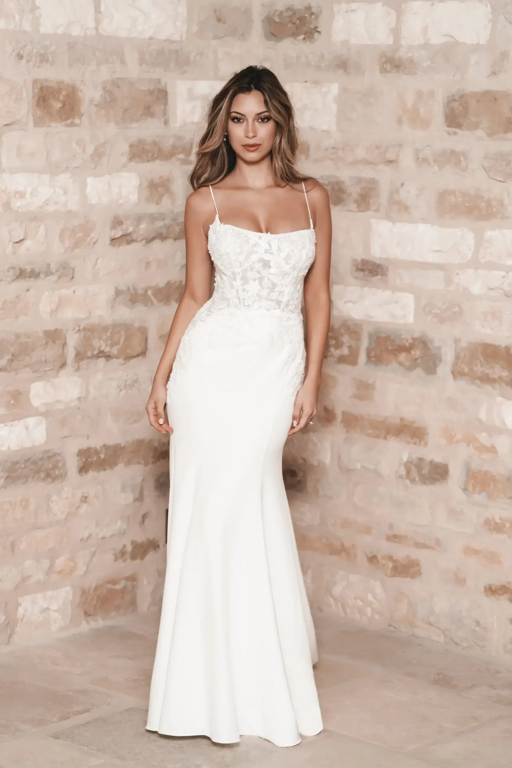 Model is wearing a sleeveless sheath wedding dress with a lace bodice