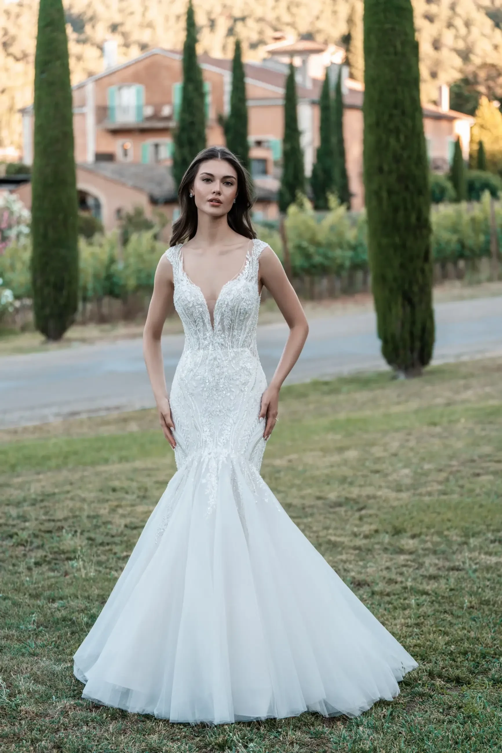 Model is wearing a sleeveless mermaid bridal gown with lace and a plunging neckline 